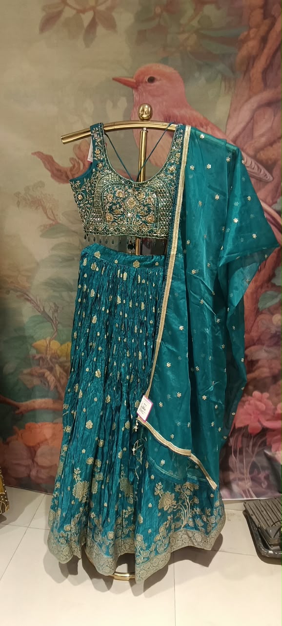 This regal three-piece teal lehenga choli royal elegance with its deep jewel tones and traditional gold artistry